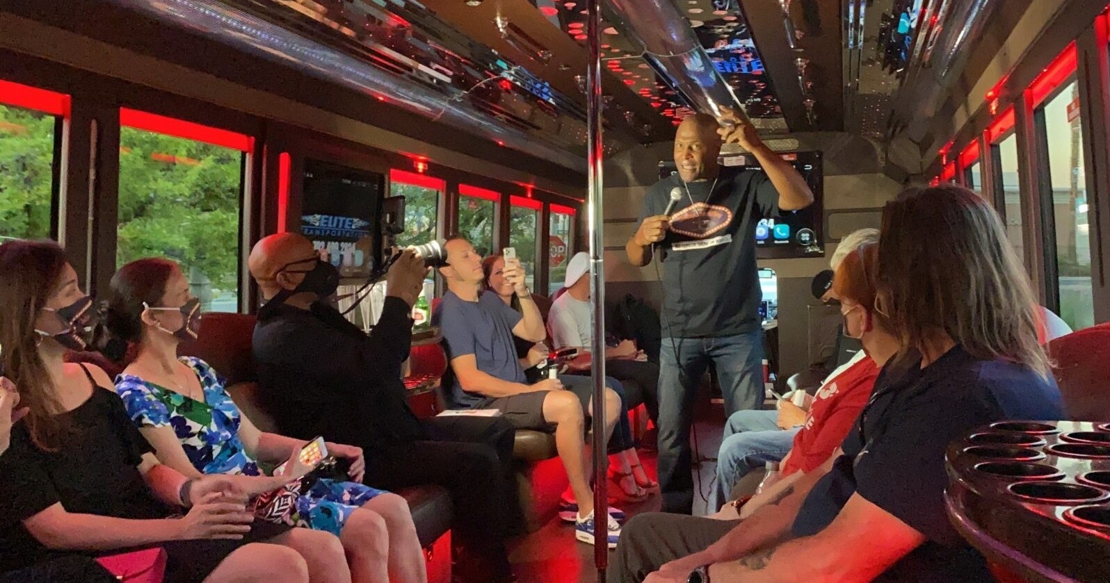 A comedian performs on a bus while the audience watches and laughs. Keeponsmilen Best Comedy Show On Wheels Comedy Show Bus Performance Audience