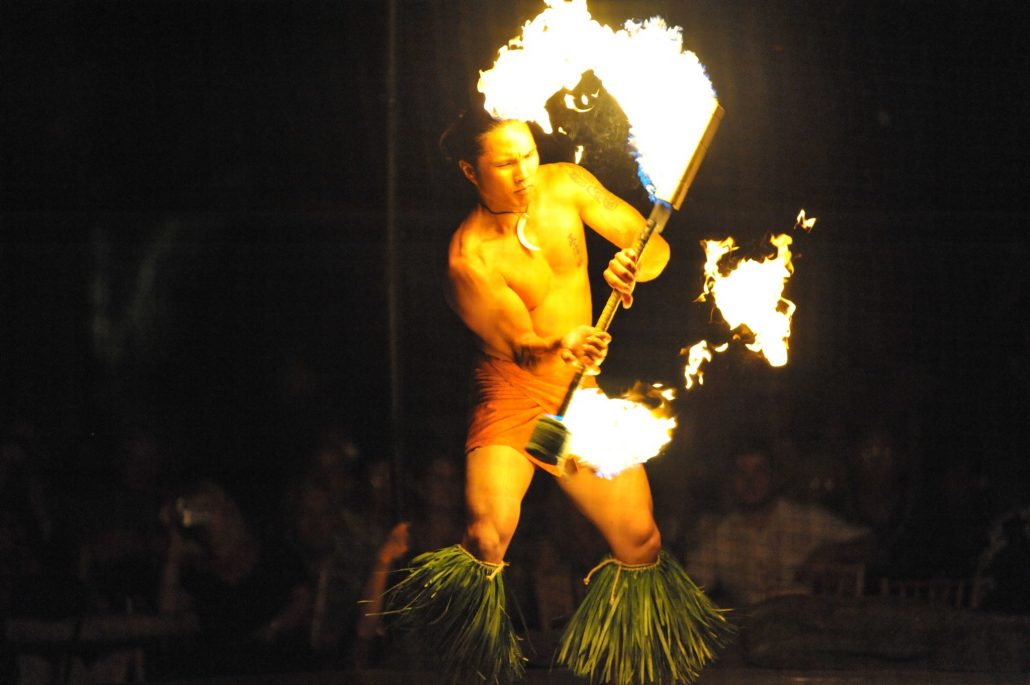 A fire dancer performs with flaming torches while wearing a grass skirt. Luau Kalamaku Hawaiian Package Fire Dancer Hula Skirt Performance