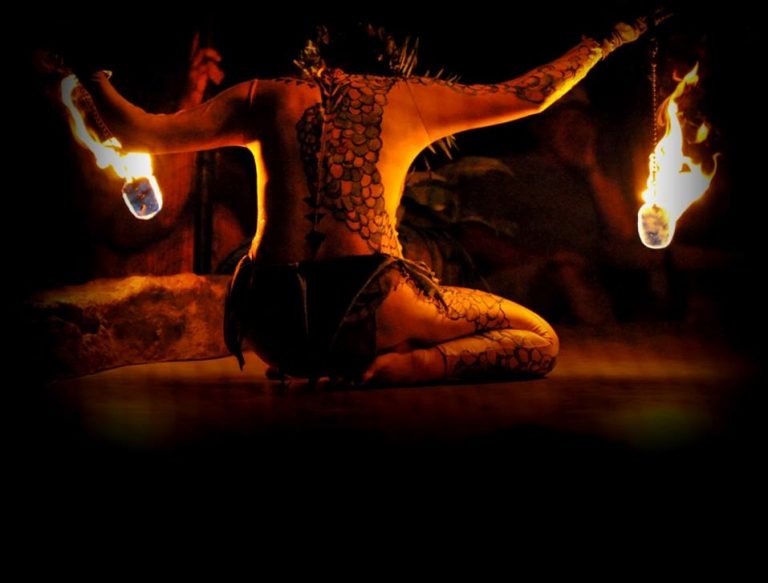 A performer with intricate tattoos spins fire torches in a dark setting. Luau Kalamaku Hawaiian Package Fire Dancer Tattoo Performance