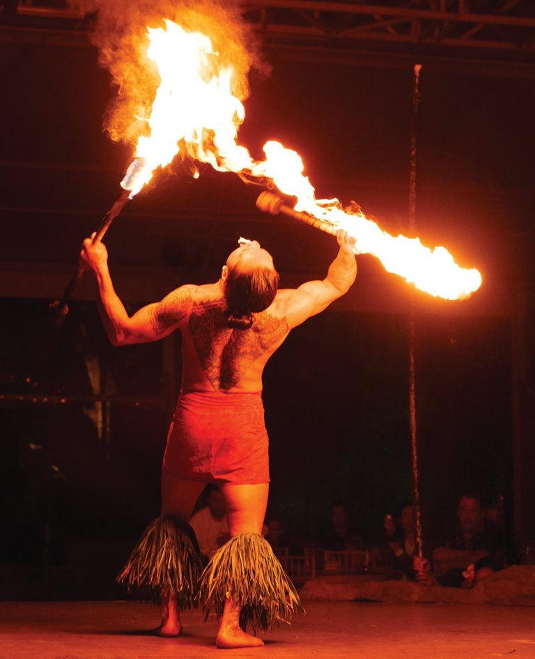 A fire dancer performs with flaming torches, showcasing intricate tattoos. Luau Kalamaku Hawaiian Package Fire Dancer Tattooed Performer Luau