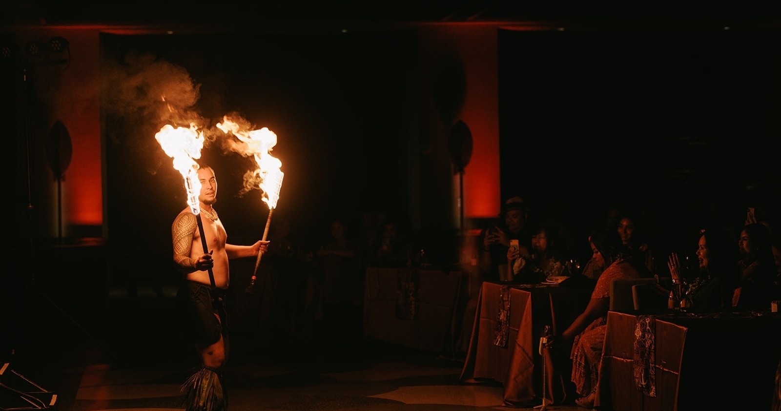 A fire dancer performs with flaming torches in a dimly lit venue. Ritzcarltonmauiluau Ohana Seating Fire Dancer Luau Performance