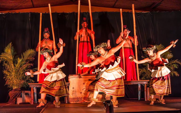Performers in traditional attire dance on stage with bamboo sticks. Ritzcarltonmauiluau Ohana Seating Luau Dancers Bamboo Sticks