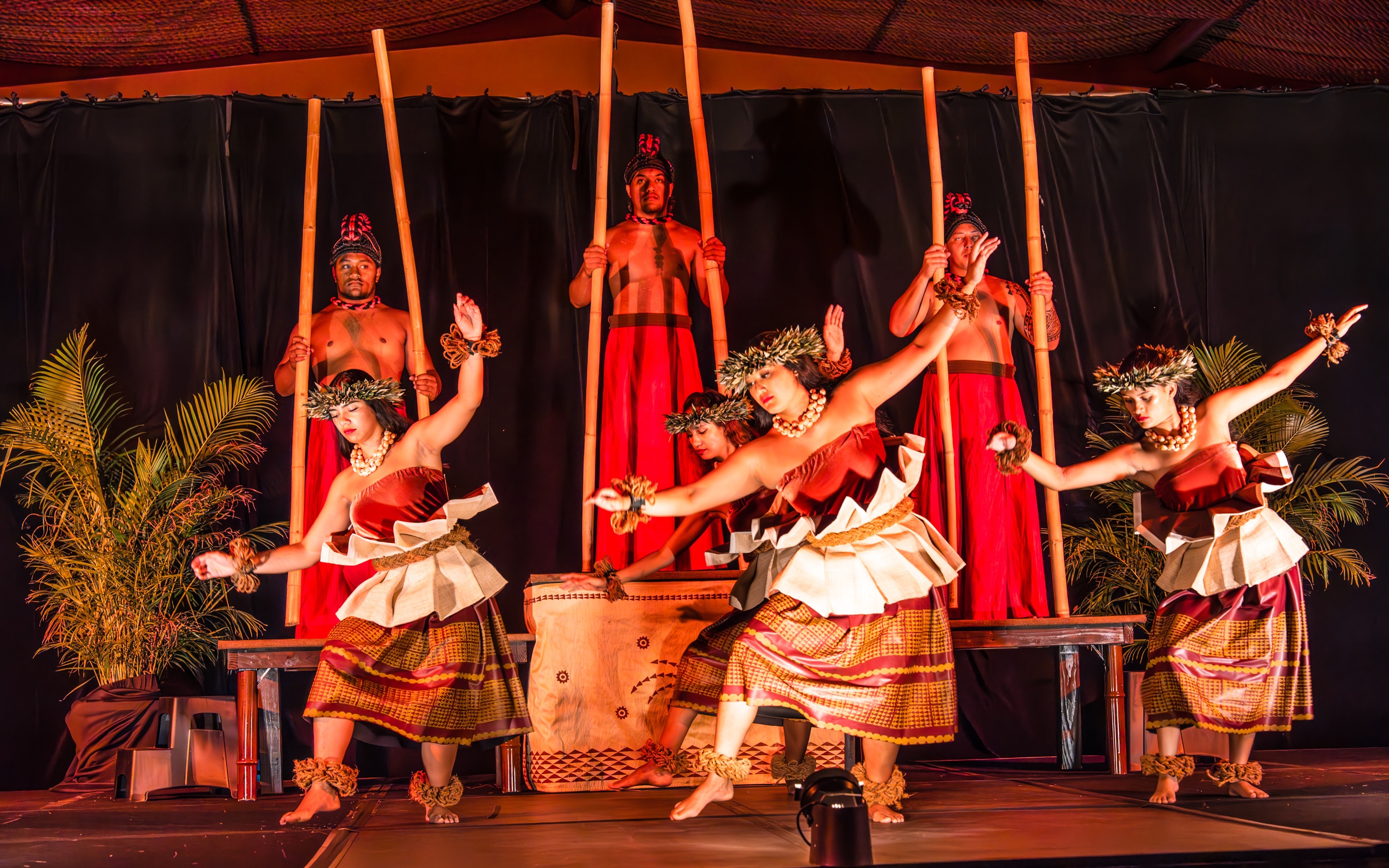 Performers in traditional attire dance on stage with bamboo sticks. Ritzcarltonmauiluau Ohana Seating Luau Dancers Bamboo Sticks