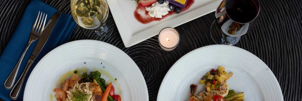 Two plates of food with vegetables, a glass of white wine, and a candle. Royalsonestaluau Drums Dances Of Polynesia At The Royal S Dinner Plates Wine Candle