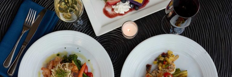 Two plates of food with vegetables, a glass of white wine, and a candle. Royalsonestaluau Drums Dances Of Polynesia At The Royal S Dinner Plates Wine Candle