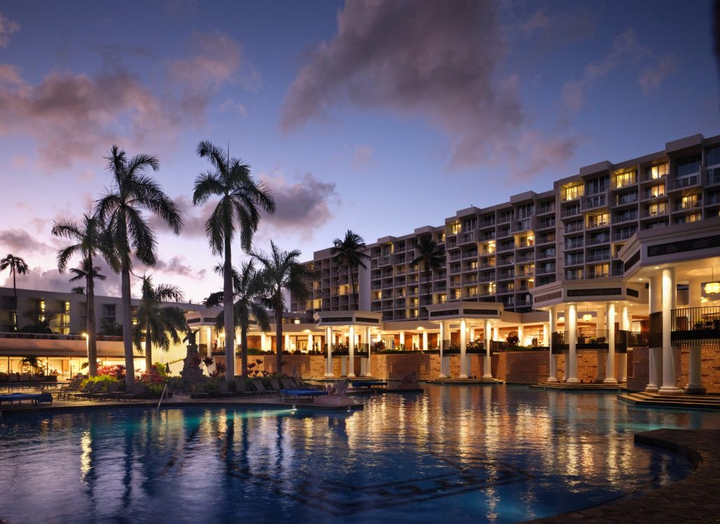 Palm trees surround a hotel pool at dusk, with lights reflecting on the water. Royalsonestaluau Drums Dances Of Polynesia At The Royal S Palm Trees Hotel Pool Dusk