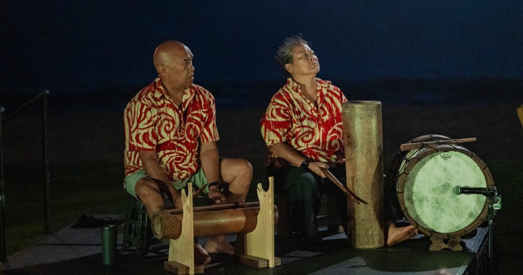 Two musicians in patterned shirts sit beside traditional drums at night. Royalsonestaluau Drums Dances Of Polynesia At The Royal S Polynesian Drummers Night Performance