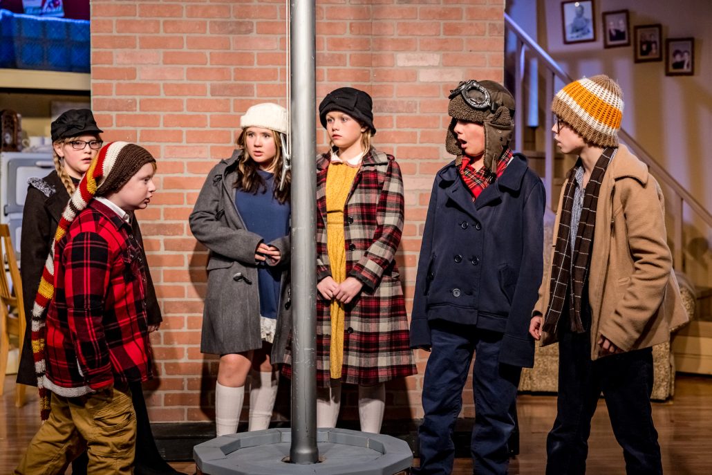 A group of children in winter costumes stands near a pole against a brick wall. Theshepherdofthehills A Christmas Story Dinner Show Children Winter Costumes Brick Wall