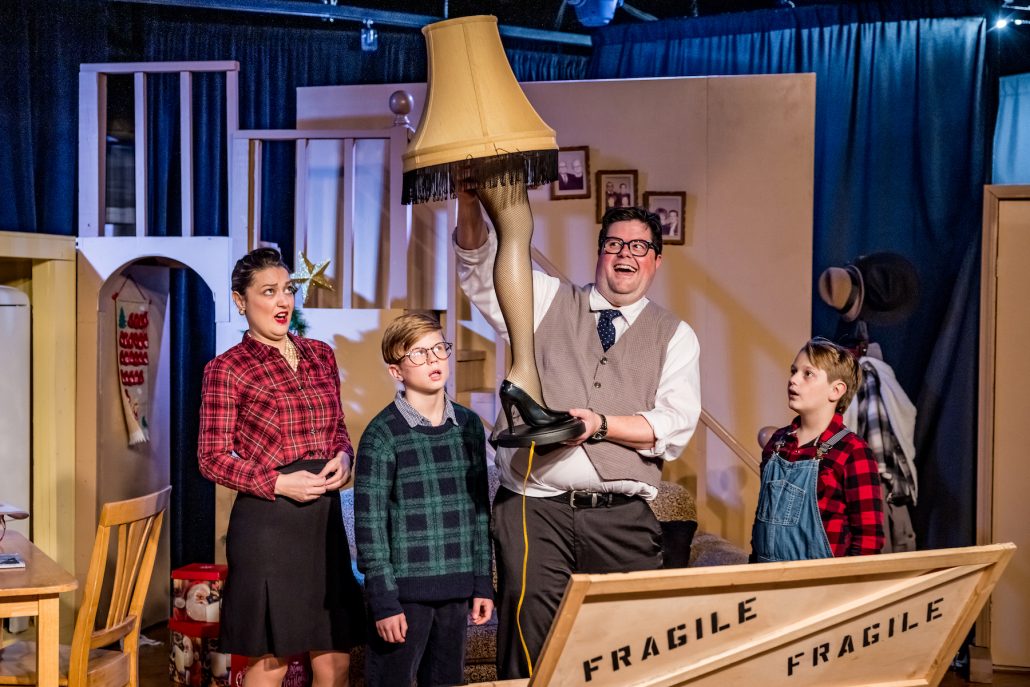A man holds a lamp shaped like a leg while others react. Theshepherdofthehills A Christmas Story Dinner Show Christmas Dinner Show Lamp Scene