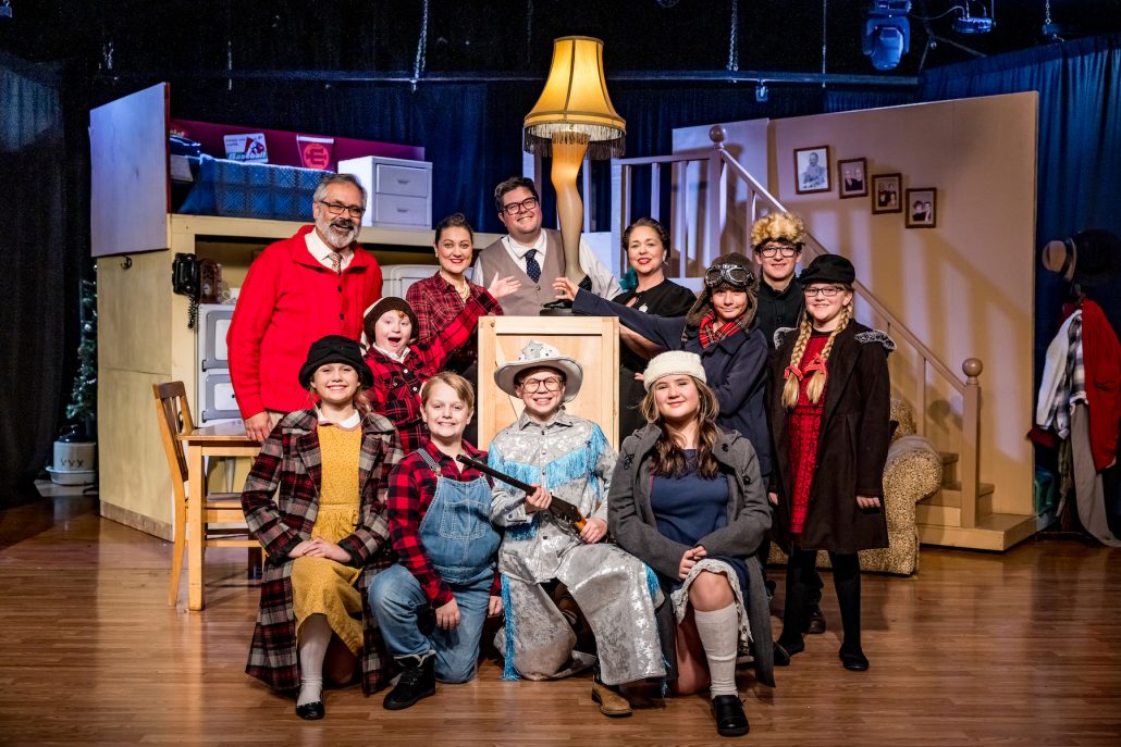 A theater cast poses around a lamp on a stage with a staircase. Theshepherdofthehills A Christmas Story Dinner Show Theater Cast Lamp Stairs Costumes