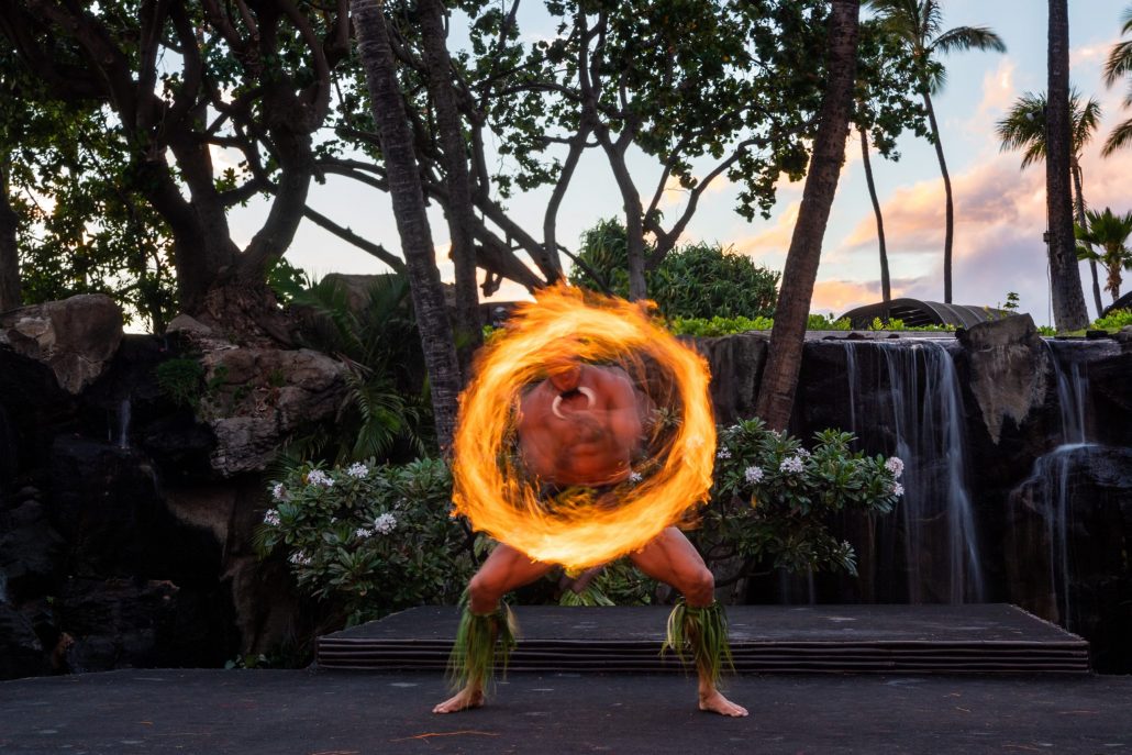 A performer spins a flaming ring on stage surrounded by tropical plants. Westinmaui Ohana Seating Fire Dancer Luau Performance