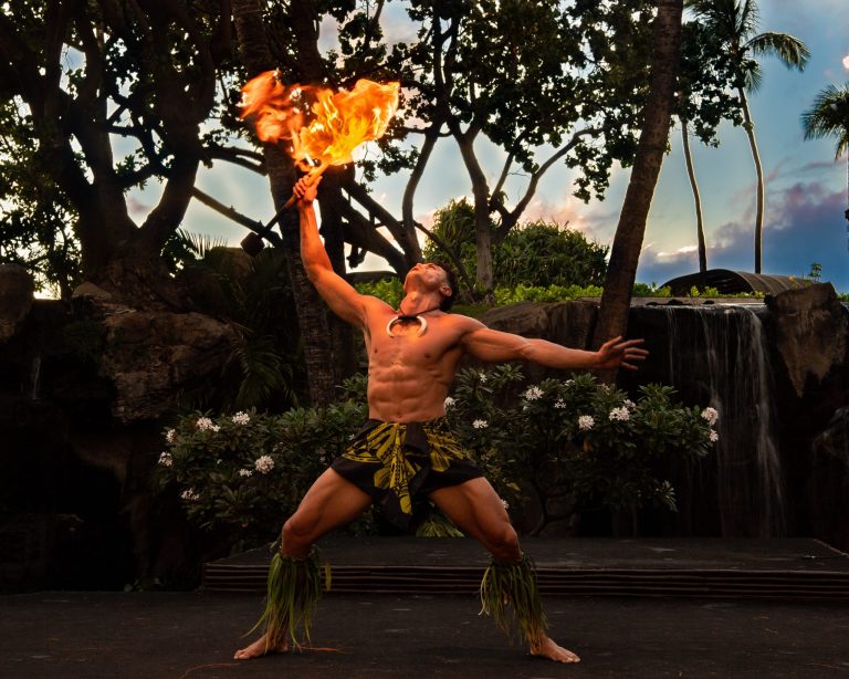 A muscular performer holds a flaming torch while dancing on stage. Westinmaui Ohana Seating Fire Dancer Performance Luau