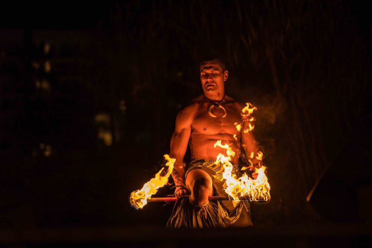 A fire dancer performs with flaming torches in a dark setting. Westinmaui Ohana Seating Fire Dancer Performance Night