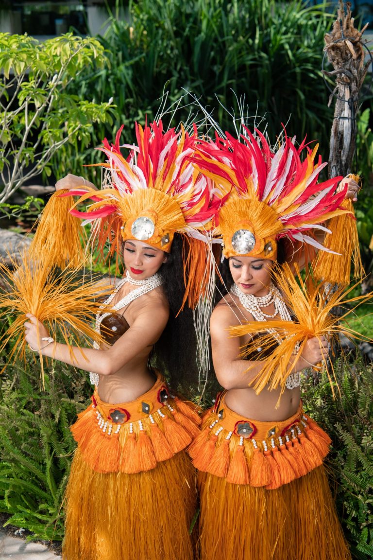 Two hula dancers in orange costumes perform with feathered headdresses. Westinmaui Ohana Seating Hula Dancers Orange Costumes